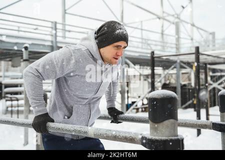 Giovane uomo atletico che fa tuffi su un bar parallelo durante il suo allenamento invernale Foto Stock