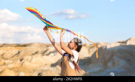 Una ragazza in un vestito estivo lancia un aquilone nel cielo nel selvaggio. Foto Stock