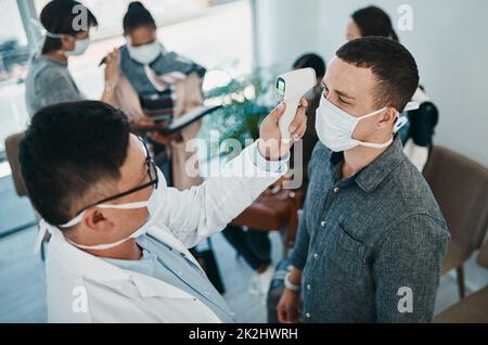 Tutto inizia con una febbre. Scatto di un giovane uomo che ottiene la sua temperatura presa con un termometro a infrarossi da un operatore sanitario durante un focolaio. Foto Stock