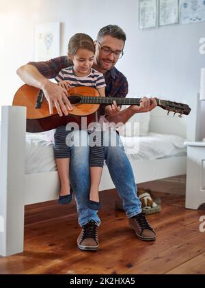 Hanno molto in comune. Scatto di una bambina che suona la chitarra con suo padre. Foto Stock