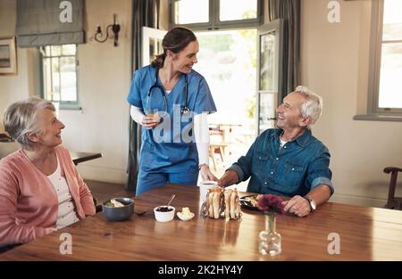 Buongiorno ai miei residenti preferiti. Shot di una giovane infermiera che controlla su una coppia anziana durante la prima colazione in una casa di cura. Foto Stock