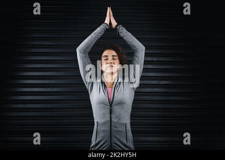 Raccogliendo energia buona dal mondo. Ripresa ritagliata di una giovane donna attraente in piedi su uno sfondo nero con le braccia sollevate in una posizione yoga. Foto Stock