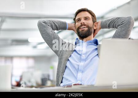 Prendendosi un momento per pensare. Scatto di un giovane uomo d'affari che lavora sul suo laptop in ufficio e si appoggia sulla sedia. Foto Stock