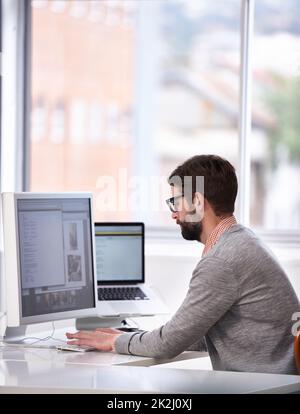 Lavorare alla prossima grande cosa. Scatto di un bel giovane uomo che lavora su un computer in un ambiente di lavoro informale. Foto Stock