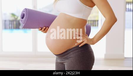 Mostrando fuori il suo bump del bambino. Scatto corto di una giovane donna incinta irriconoscibile che porta un tappeto yoga. Foto Stock