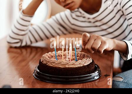 Compleanni in quarantine...not fresco. Scatto corto di una donna che illumina le candele su una torta di compleanno a casa e sembra triste. Foto Stock