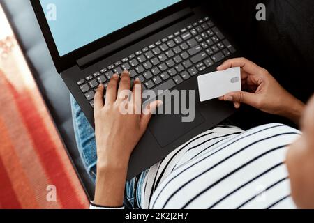 Non è più facile di questo. Scatto ritagliato di una donna utilizzando un computer portatile e una carta di credito sul divano a casa. Foto Stock