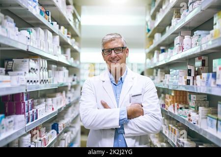 Im sicuro che youll ottenere migliore con me per aiutarla. Ritratto di un farmacista maschile maturo allegro in piedi con le braccia ripiegate mentre guarda la macchina fotografica in una farmacia. Foto Stock