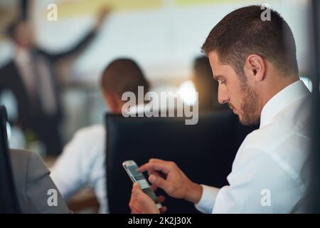 Prendere appunti sul suo smartphone. Scatto corto di un giovane uomo d'affari usando il suo cellulare mentre si siede nella sala riunioni. Foto Stock