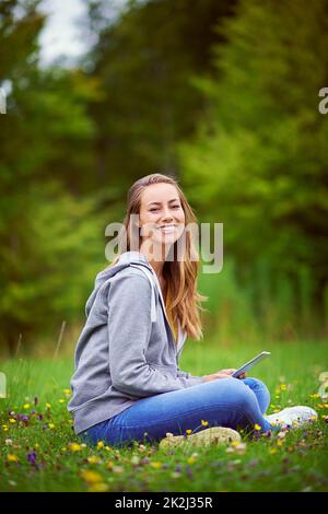 Mescolando natura e tecnologia. Scatto di una giovane donna con il suo tablet digitale al parco. Foto Stock