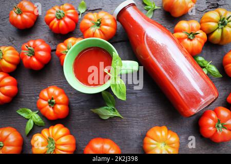 Composizione piatta con bottiglia di succhi freschi su sfondo di legno scuro con pomodori rossi e foglie di basilico Foto Stock