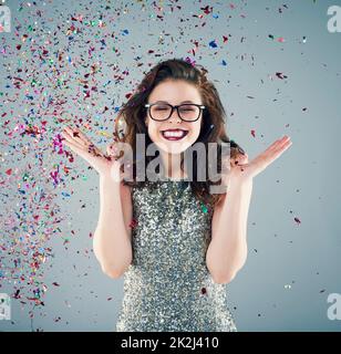 Lancia alcuni confetti nell'aria e festeggia. Studio girato di una giovane donna con confetti che cadono intorno a lei su uno sfondo grigio. Foto Stock