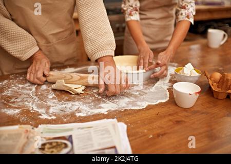Realizzato con amore... Una vista ritagliata delle mani che lavorano l'impasto mentre si cuoce in cucina. Foto Stock