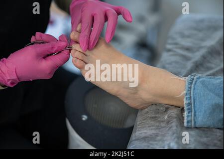 Il podiatrist fa un pedicure ad un cliente. Il padrone conduce l'igiene delle dita dei piedi con un bastone di metallo. Foto Stock