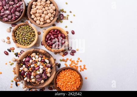 Vista dall'alto di diversi fagioli, lenticchie, mung, ceci in ciotole di legno per gustosi pasti su sfondo grigio cemento Foto Stock