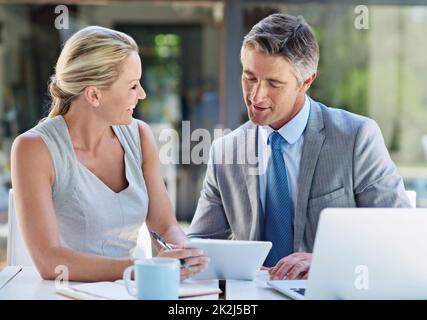 Utilizzo di ogni dispositivo a loro disposizione. Due uomini d'affari maturi che parlano insieme di un tablet e di un notebook. Foto Stock