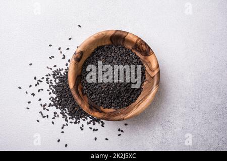 Vista dall'alto dei semi di sesamo nero in una piccola ciotola di legno come ingrediente per cibi sani e gustosi su fondo grigio in cemento Foto Stock