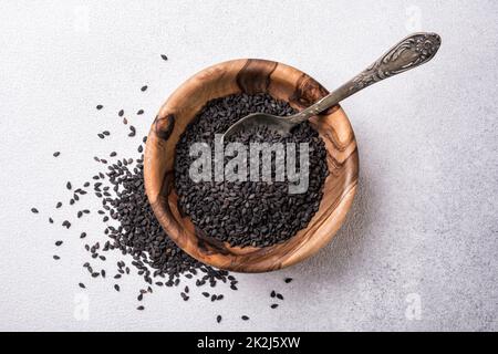 Vista dall'alto dei semi di sesamo nero in una piccola ciotola di legno come ingrediente per cibi sani e gustosi su fondo grigio in cemento Foto Stock