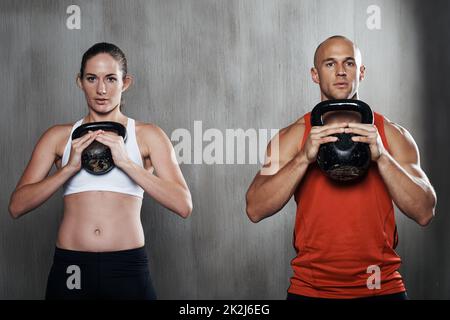 Si impegnano a mantenere la forma. Un uomo e una donna che si allenano con le campane del bollitore in palestra. Foto Stock