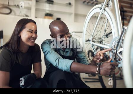 Ho risolto questo. Girato di due giovani proprietari di affari accovacciati nel loro negozio e fissare una ruota di bicicletta. Foto Stock