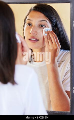 Pulizia prima di coricarsi. Scatto di una bella giovane donna che guarda nello specchio mentre pulisce il suo viso. Foto Stock