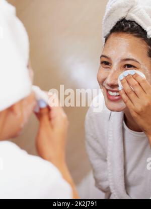 Conosco alcuni trucchi quando viene a realizzare la pelle perfetta. Scatto di una bella giovane donna che guarda nello specchio mentre pulisce il suo viso. Foto Stock