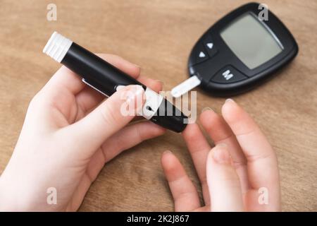 Le mani del bambino che usano Lancet sul dito per controllare il livello di zucchero nel sangue con il glucometro. Foto Stock