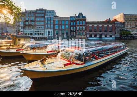 Barche turistiche ormeggiate nel molo dei canali di Amsterdam al tramonto Foto Stock