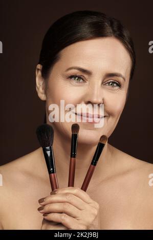 Bella donna di mezza età con un makeup spazzole su sfondo marrone Foto Stock