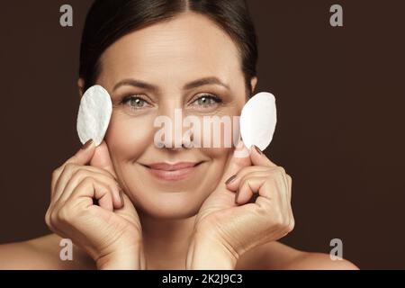 Bella donna di mezza età con un tampone di cotone per la pulizia del viso o la routine di rimozione del make-up Foto Stock
