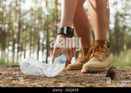 Escursionista femmina che raccoglie rifiuti di plastica nella foresta verde Foto Stock