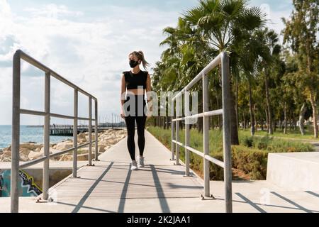 Donna che indossa la maschera facciale durante il suo allenamento estivo di strada Foto Stock