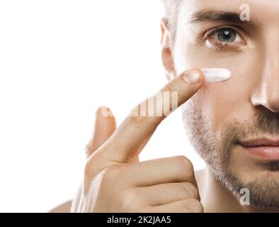 La bellezza degli uomini. Giovane uomo sta applicando crema idratante e anti invecchiamento sul suo viso Foto Stock