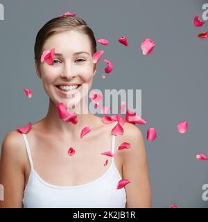 I thats di bellezza come freschi come un burst dei fiori. Ritratto studio di una giovane donna attraente circondato da petali rosa caduta su uno sfondo grigio. Foto Stock