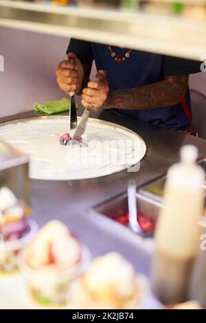 Lavorando la sua magia del cibo. Shot di un fornitore di cibo non identificabile che prepara un dolce in una bancarella del mercato. Foto Stock