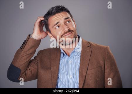 Bello ed elegante. Studio girato di un uomo graffiando la sua testa su uno sfondo grigio. Foto Stock