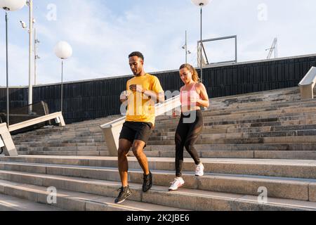Allenamento sportivo interrazziale di coppia all'aperto - coppia multirazziale indossando abbigliamento sportivo e facendo allenamento funzionale all'aperto per tendere i muscoli del corpo, Foto Stock
