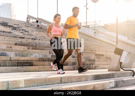 Allenamento sportivo interrazziale di coppia all'aperto - coppia multirazziale indossando abbigliamento sportivo e facendo allenamento funzionale all'aperto per tendere i muscoli del corpo, Foto Stock