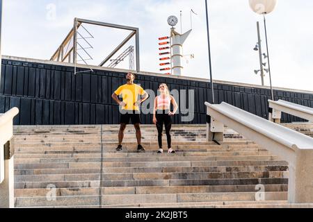 Allenamento sportivo interrazziale di coppia all'aperto - coppia multirazziale indossando abbigliamento sportivo e facendo allenamento funzionale all'aperto per tendere i muscoli del corpo, Foto Stock