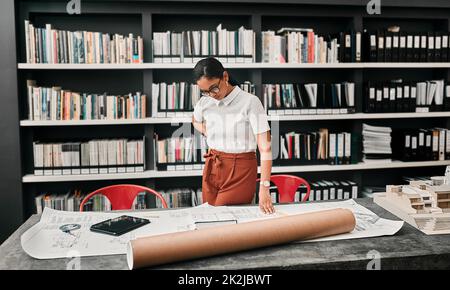 Questi richiedono la sua piena attenzione. Scatto ritagliato di un attraente giovane architetto femminile che lavora con i progetti in un ufficio moderno. Foto Stock