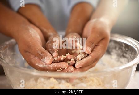 I bambini imparano sporcarsi. Il colpo corto di un padre e di un figlio irriconoscibili che ricoprono le loro mani in pastella dei biscotti mentre cuocete insieme a casa. Foto Stock