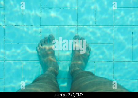Foto subacquee, il fondo della piscina con piastrelle blu, gambe uomo in piedi su di esso. Foto Stock