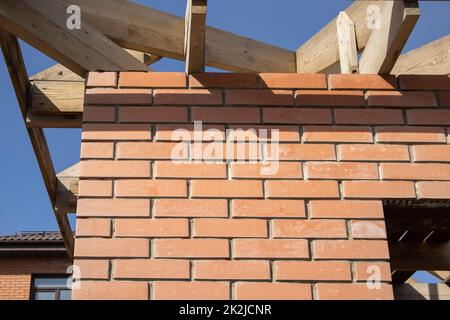 Un edificio residenziale privato in costruzione con una struttura di tetto in legno. Costruzione in mattoni incompiuta, primo piano Foto Stock