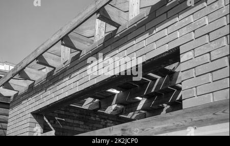 Foto in bianco e nero, un edificio residenziale privato in costruzione con una struttura di tetto in legno. Costruzione in mattoni incompiuta, primo piano Foto Stock