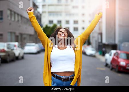 È fantastico essere giovani e vivi. Scatto corto di una giovane donna felice che festeggia con le armi sollevate su uno sfondo di città. Foto Stock