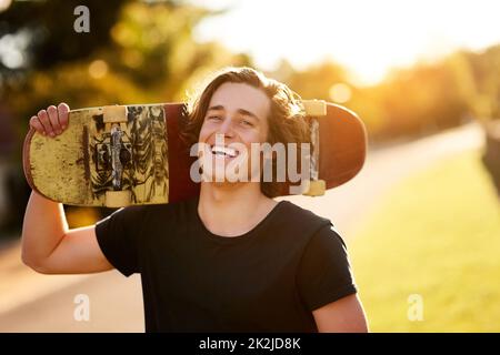 Naturalmente pattinare mi fa sembrare fresco. Ritratto di un giovane uomo in piedi con il suo skateboard fuori. Foto Stock