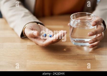 Spero che questi aiuti. Scatto corto di una donna d'affari irriconoscibile che prende le pillole con un vetro di acqua mentre nel suo ufficio. Foto Stock