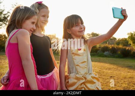 Ci sembra troppo carino per non prendere un selfie insieme. Scatto corto di un gruppo di ragazze piccole che prendono un selfie insieme fuori. Foto Stock