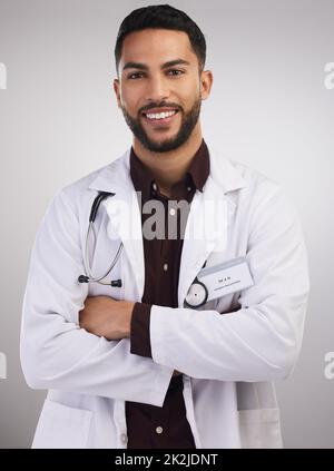 Im qui per farti sentire meglio. Scatto di un bel medico giovane in piedi da solo nello studio con le braccia ripiegate. Foto Stock