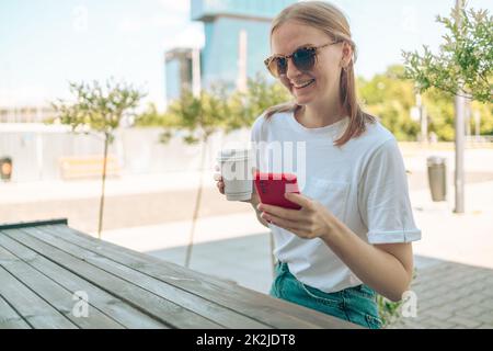 Primo piano di una giovane donna caucasica che tiene in mano utilizzando smartphone cellulare per e-banking lavoro remoto mentre si beve caffè nel bar ristorante Foto Stock
